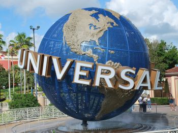 A large globe sculpture with "UNIVERSAL" in bold letters, surrounded by palm trees and people taking photos in the background.