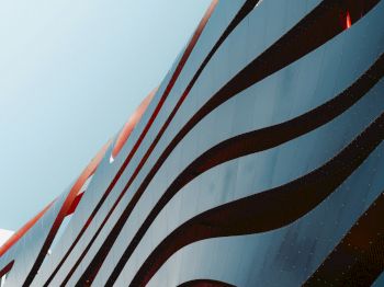 A building facade with flowing red and silver lines, creating a dynamic, wave-like appearance against a clear sky.
