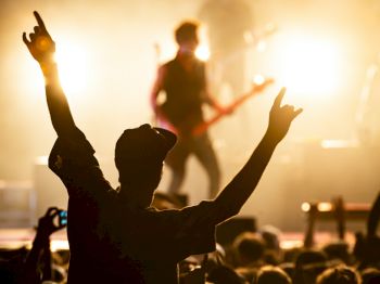 A concert scene with a crowd and a person raising their hands in front of a lit stage with musicians performing.