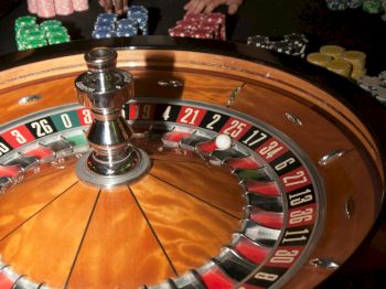 A roulette table with a spinning wheel and casino chips being handled by people.