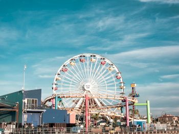 A Ferris wheel stands tall over a pier, with colorful surroundings and a clear blue sky above, capturing a vibrant amusement park scene.