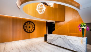 A modern and sleek interior with a marble reception desk, a large wall clock, spiral wooden accents, and hanging light fixtures.