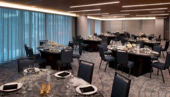 An elegantly decorated banquet hall with round tables set for a formal event, featuring black chairs, glassware, and flower centerpieces.