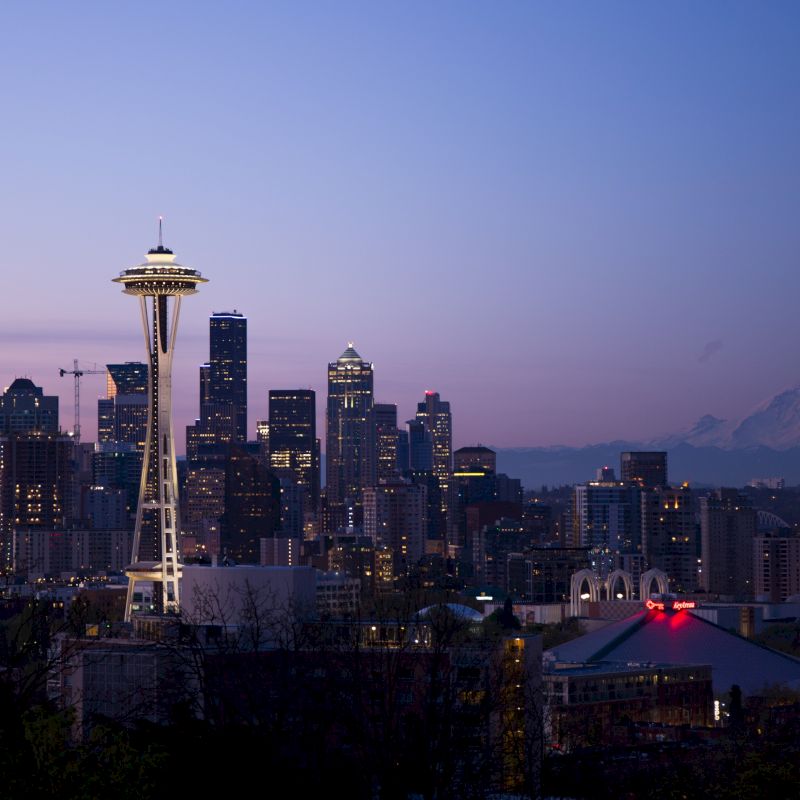 This image shows the Seattle skyline at dusk, featuring the Space Needle, various skyscrapers, and Mount Rainier in the background.