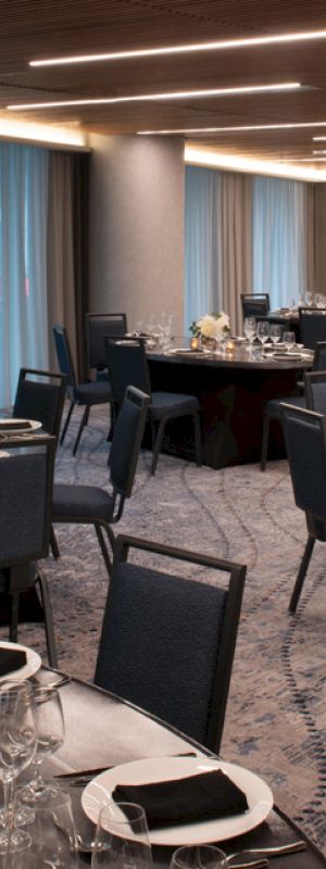 A banquet hall with round tables set for an event, featuring black chairs, elegant table settings with flowers, and modern ceiling lighting.