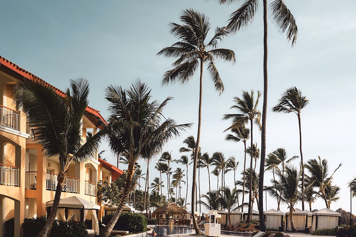 A tropical resort pool area with lounge chairs, palm trees, and a building on the left under a clear sky completes the serene setting.